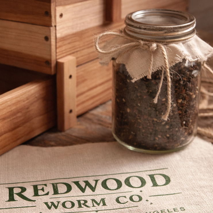 Jar of soil with a label on a Redwood Worm Co. bag on a wooden surface